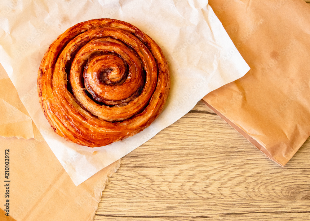 A baked cinnamon roll on white and brown paper. The close-up food photo. A baked cinnamon roll on white and brown paper. The close-up food photo.