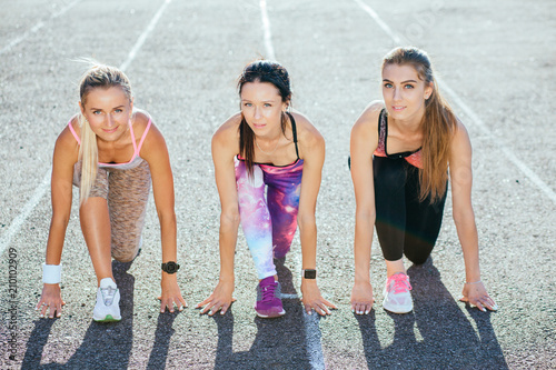 Three beautiful girls is ready to run. Group spoty women on stadium track in sunny summer morning. Healthy lifestyle concept. photo