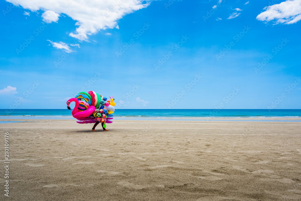 A dealer in inflatable swimming circles walks along the beach
