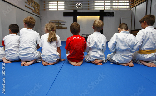 Children sitting with their backs before starting aikido training. A boy in a red T-shirt in the middle with the inscription: Poland photo