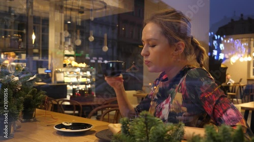 Girl eating her sandwich and drink cofee sitting behind the glass frontage in cafe bistro, the view fromm street photo