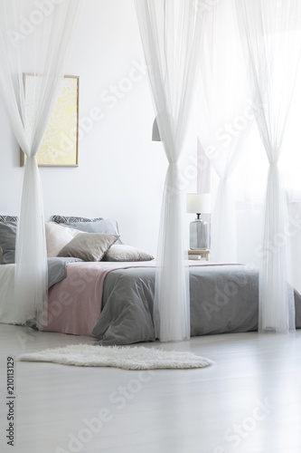 Bright bedroom interior with glass lamp, gold poster on the wall and double bed with grey bedding and many pillows