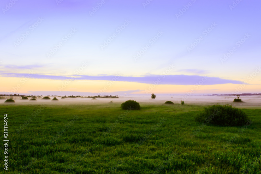Countryside landscape of the colorful sky and steam fog above meadows just before sunrise.
