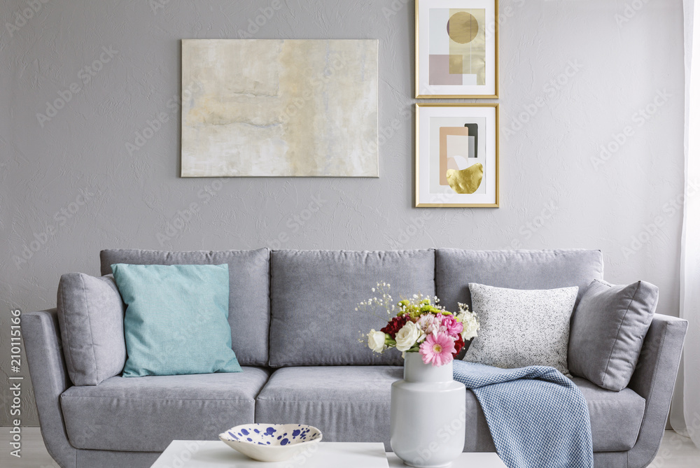 Modern painting and two gold posters hanging on the wall in grey sitting room interior with sofa with pillows and fresh colorful flowers in ceramic vase - obrazy, fototapety, plakaty 