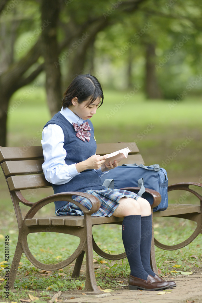 ベンチに座って本を読む女子校生