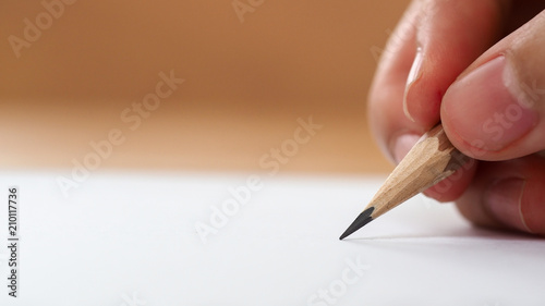 Closeup student hand holding pencil writing on paper with blurred background, business and education background