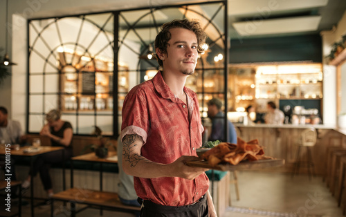 Young waiter holding a platter of freshly baked nachos