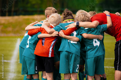 Boys football team with coach. Youth soccer team huddle with coach. Motivation talk, pep talk before the match. Young football soccer players in jersey colorful sportswear