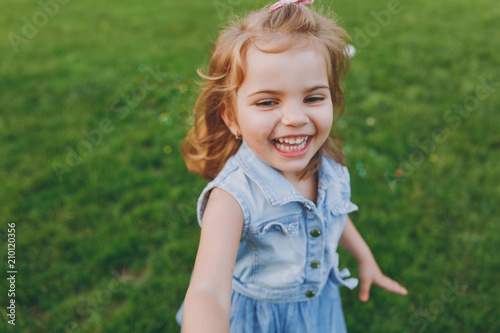 Joyful little cute child baby girl in denim dress walking and running, have fun on green grass lawn in park. Mother, little kid daughter. Mother's Day, love family, parenthood, childhood concept.