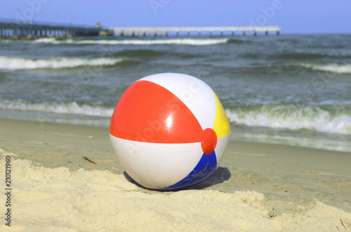 Colorful beach ball on sand and waving sea. Holiday beach ball near Baltic sea and Palanga bridge in horizon.