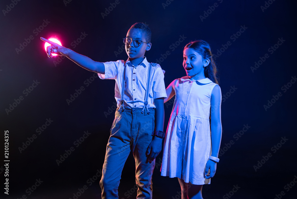 Fototapeta premium Amazement. Cheerful afro-american boy pressing imaginary buttons and a surprised girl standing near him