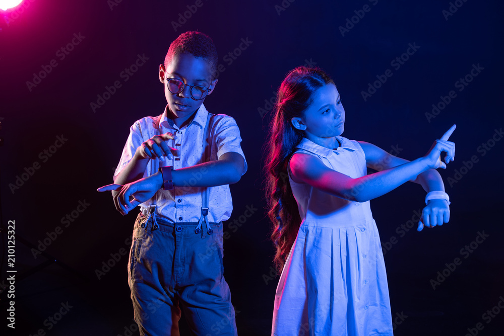 Setting the time. Serious afro-american boy looking at his watch and a girl pressing imaginary buttons