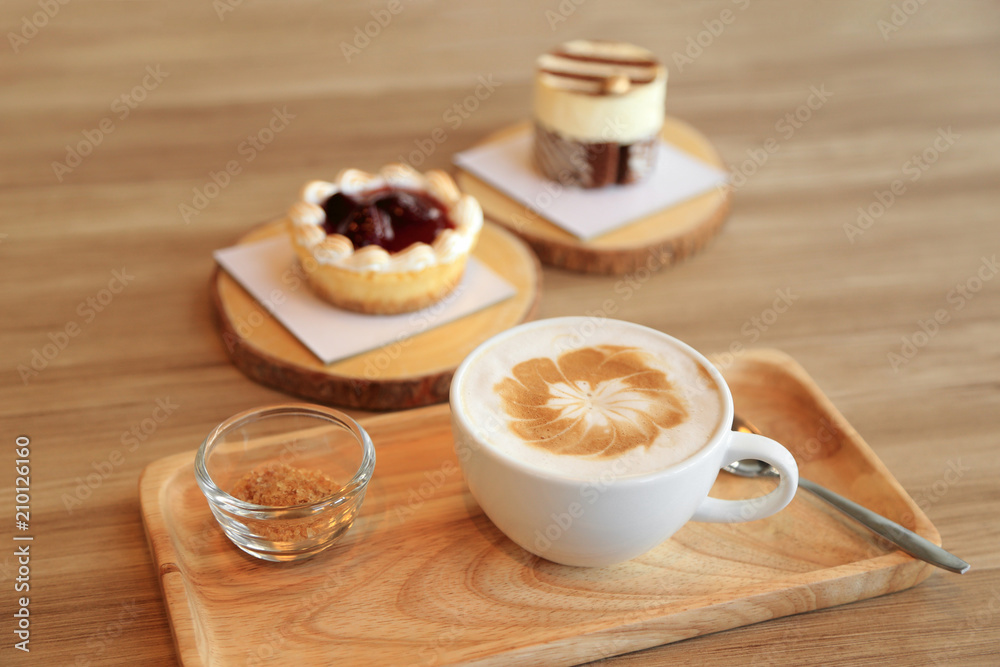 Confectioners atmosphere concept. Cup of hot latte coffee on wooden table with some of cake dessert at background. Confectioners atmosphere concept. Cup of hot latte coffee on wooden table with some of cake dessert at background.