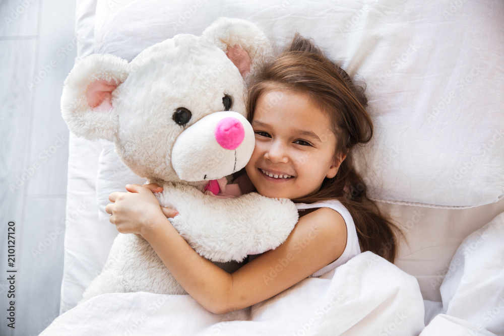 beautiful little girl hugging her teddy bear in bed