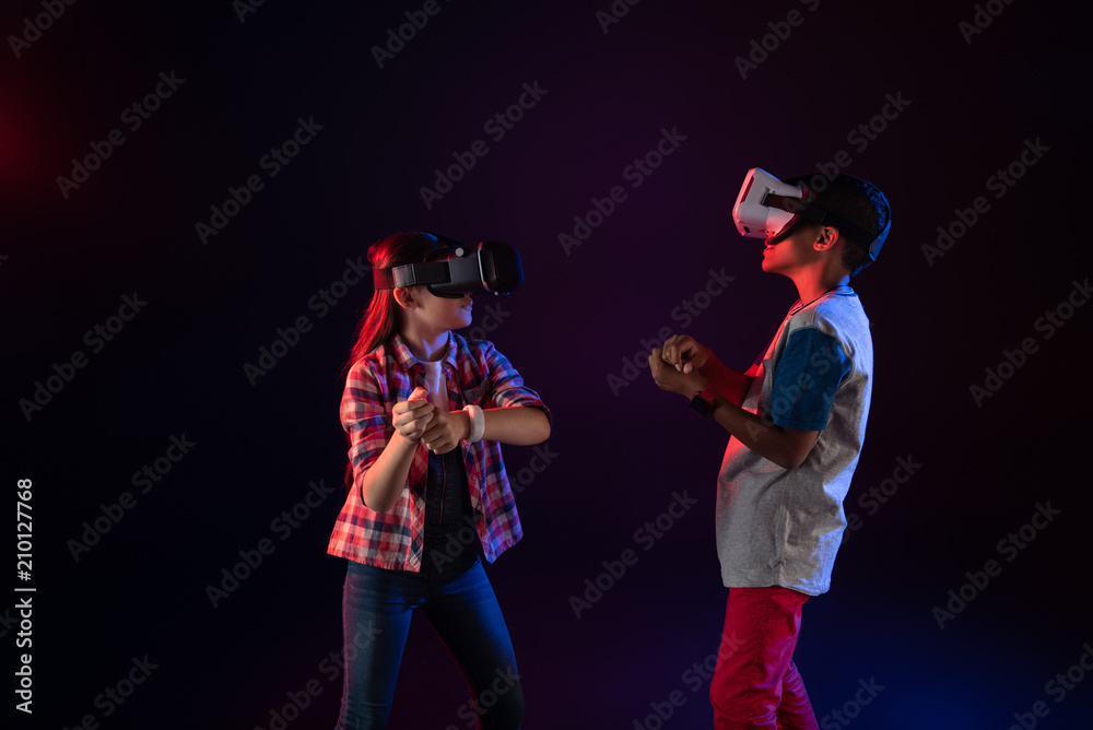 Fototapeta premium Interesting game. Concentrated little girl and a boy wearing VR headsets and playing