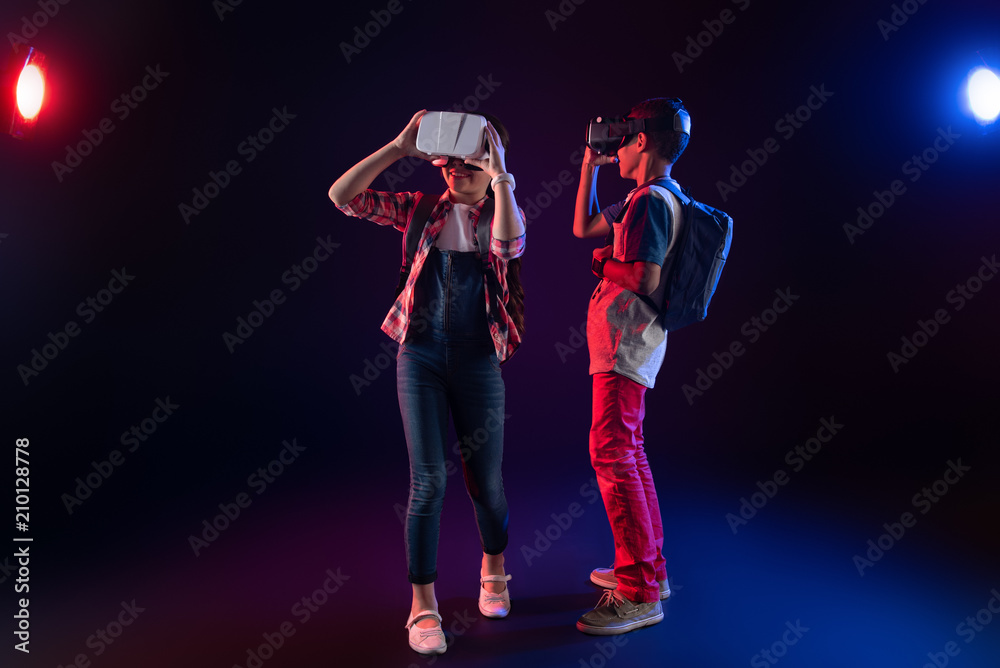 Fototapeta premium Lovely day. Smiling sweet girl and a boy wearing VR headsets and having their schoolbags on