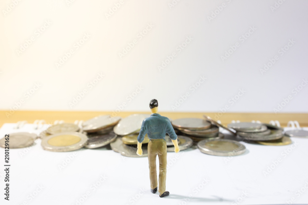 A miniature business man on paper walking into coins closeup.