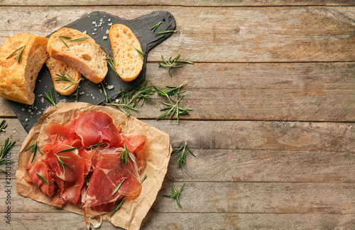 Sliced prosciutto with rosemary and bread on wooden table