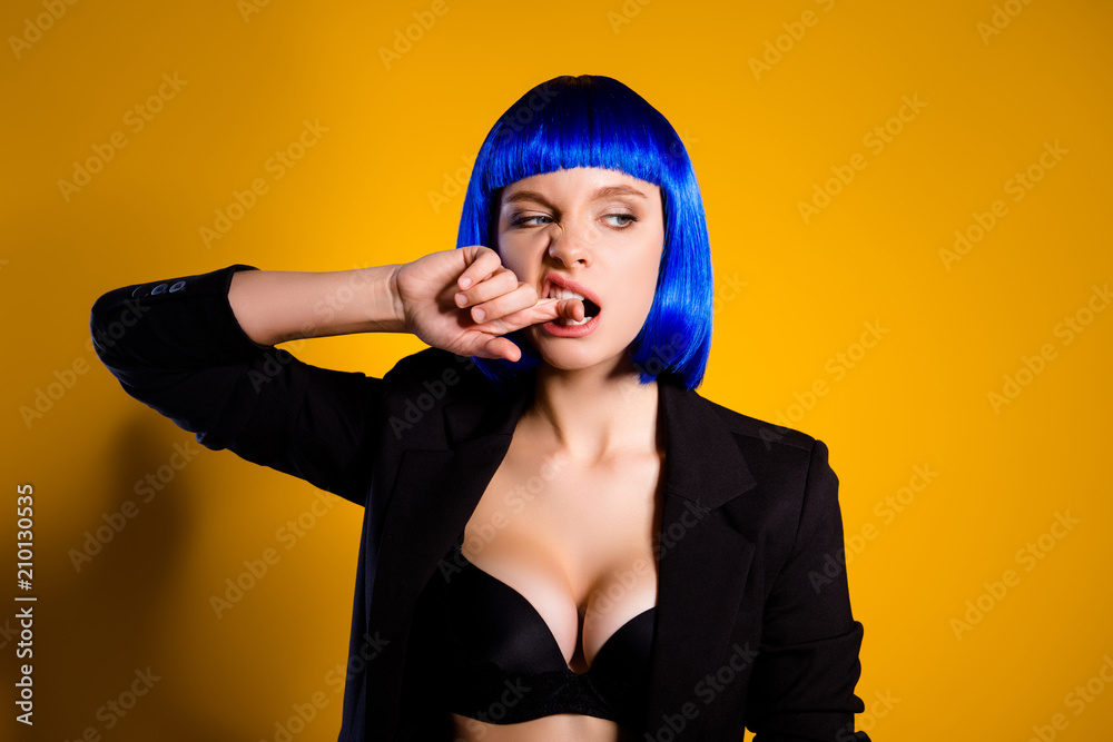 Portrait of harsh brutal woman in black jacket bright blue wig with big tits biting forefinger looking to the side isolated on yellow background. Holiday theme party dress-code concept Portrait of harsh brutal woman in black jacket bright blue wig with big tits biting forefinger looking to the side isolated on yellow background. Holiday theme party dress-code concept