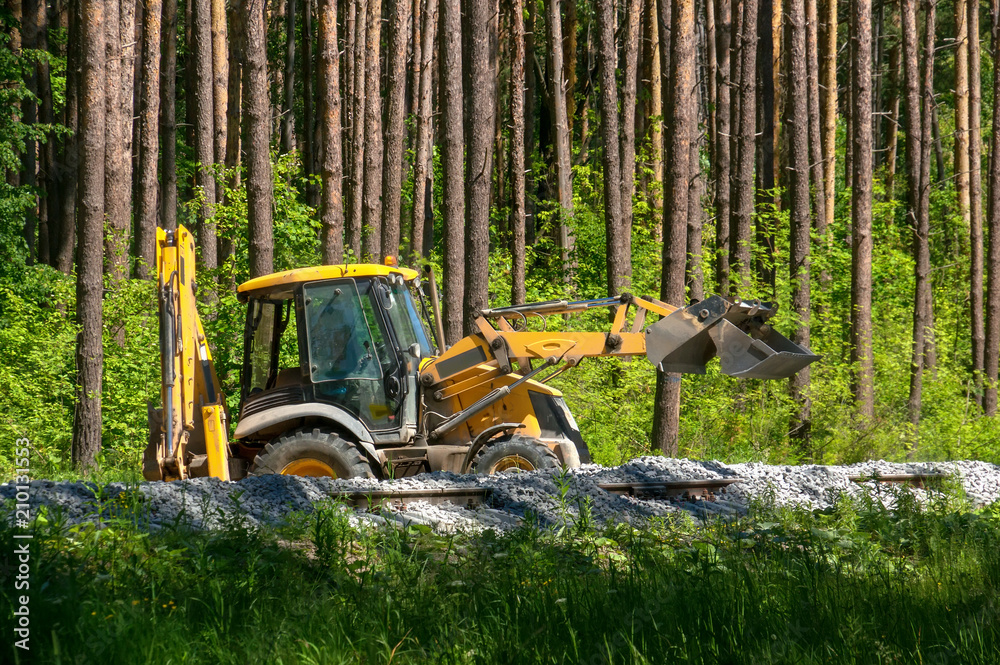 Yellow excavator pours gravel on the construction of the railway in the forest Yellow excavator pours gravel on the construction of the railway in the forest