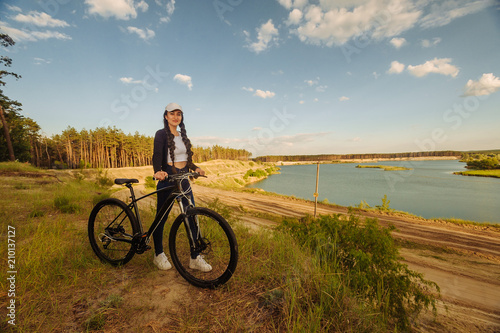 The beautiful girl is standing by bicycle. Senior woman riding a bike beside a lake. A female biker take a rest after biking © vitleo