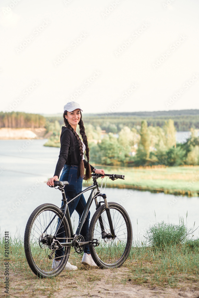 The beautiful girl is standing by bicycle. Senior woman riding a bike beside a lake. A female biker take a rest after biking