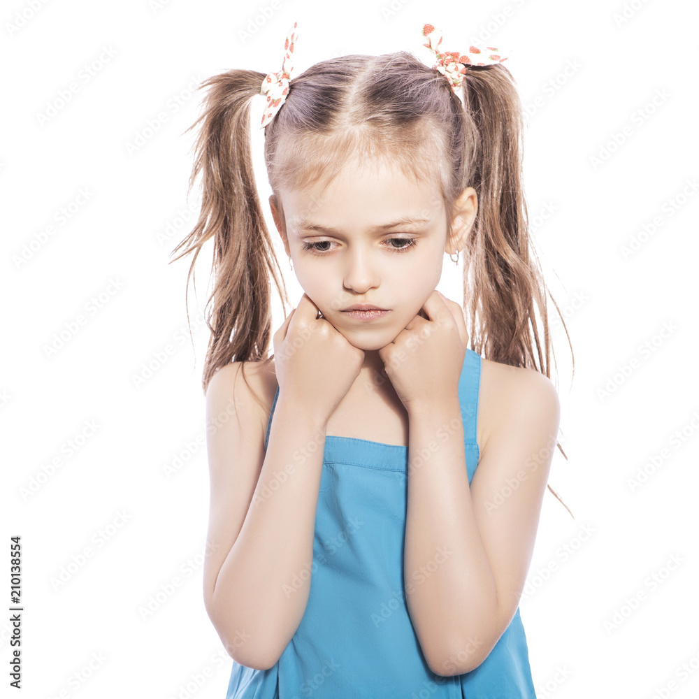 Young seven years old brunette girl in blue dress on a white isolated background. Unhappy, sad emotions on her face Young seven years old brunette girl in blue dress on a white isolated background. Unhappy, sad emotions on her face