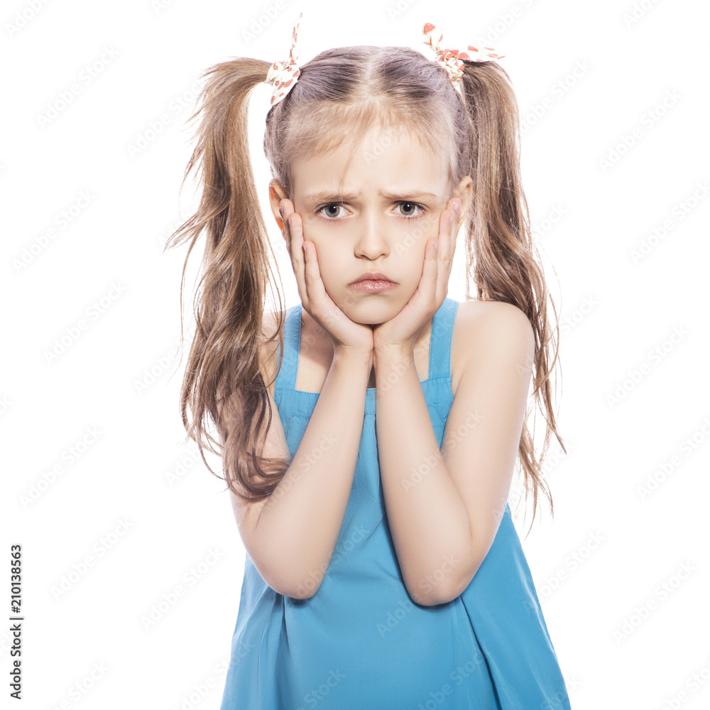Young seven years old brunette girl in blue dress on a white isolated background. Unhappy, sad emotions on her face Young seven years old brunette girl in blue dress on a white isolated background. Unhappy, sad emotions on her face