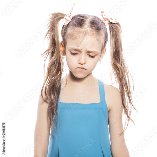Young seven years old brunette girl in blue dress on a white isolated background. Unhappy, sad emotions on her face