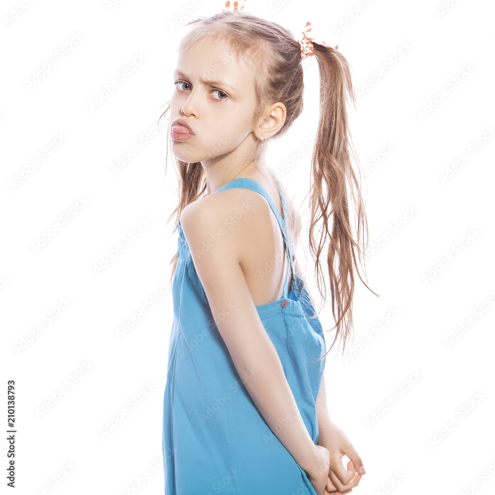 Young seven years old brunette girl in blue dress on a white isolated background. Angry, unhappy, sad emotions on her face Young seven years old brunette girl in blue dress on a white isolated background. Angry, unhappy, sad emotions on her face