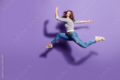 Portrait of fit sporty girl jumping over in the air looking at camera having good stretching isolated on violet background, people life energy lifestyle powerful concept