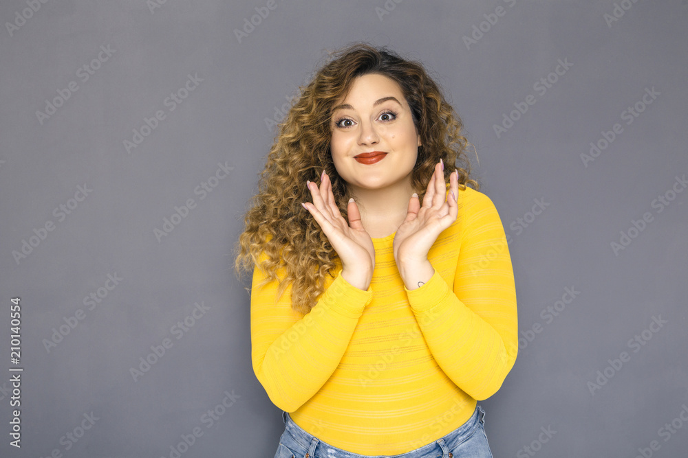 Cute brunette plus size woman with curly hair in yellow sweater and jeans standing on a neutral grey background. She amazed, shocked about some surprise Cute brunette plus size woman with curly hair in yellow sweater and jeans standing on a neutral grey background. She amazed, shocked about some surprise