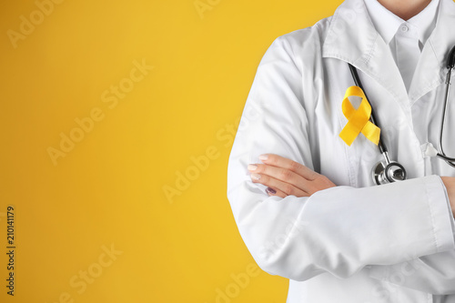 Doctor with yellow ribbon on robe against color background. Cancer awareness concept photo