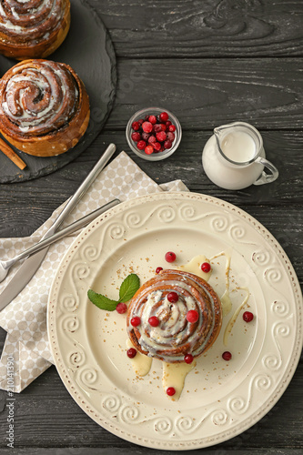 Plate with tasty cinnamon bun and jug of milk on wooden table