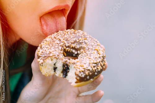 Beautiful young girl with pink donut in the open air. Fashionable hipster model in heart-shaped sunglasses. Close-up
