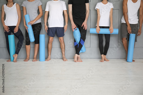 Group of sporty people with yoga mats near grey wall
