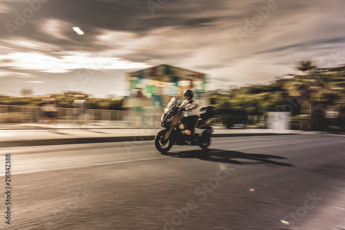 Man driving his scooter in the city with fast effect in the background.