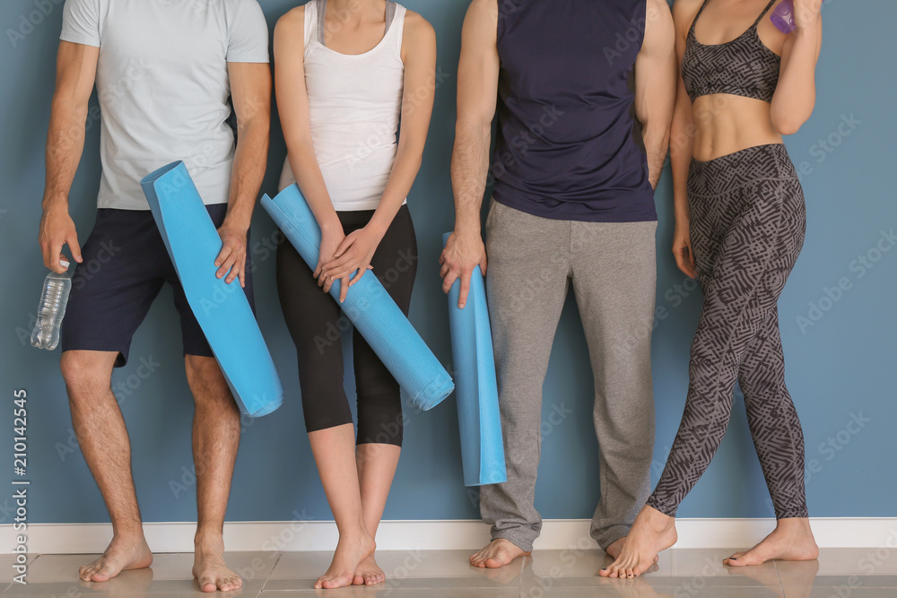 Group of people with yoga mats near color wall