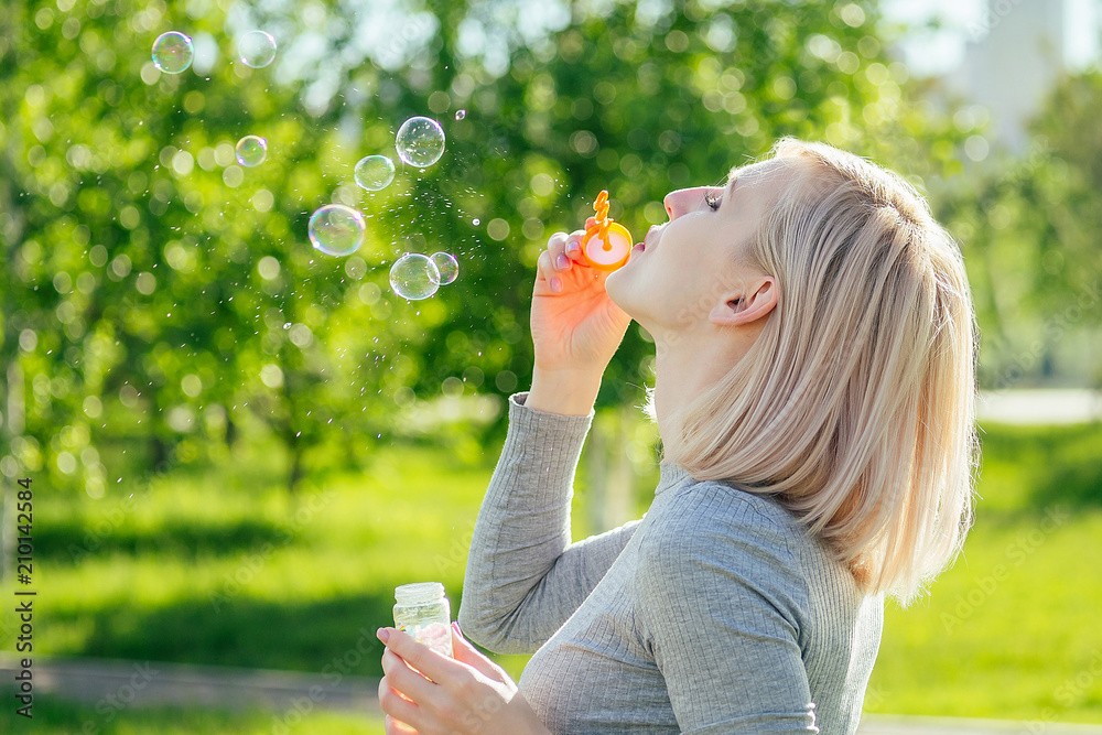 attractive blonde girl blowing soap bubbles in the park on a background of green grass . bubble and holiday atmosphere attractive blonde girl blowing soap bubbles in the park on a background of green grass . bubble and holiday atmosphere