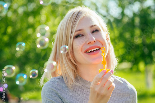 attractive blond woman blowing soap bubbles in the park on a background of green grass . bubble and holiday atmosphere