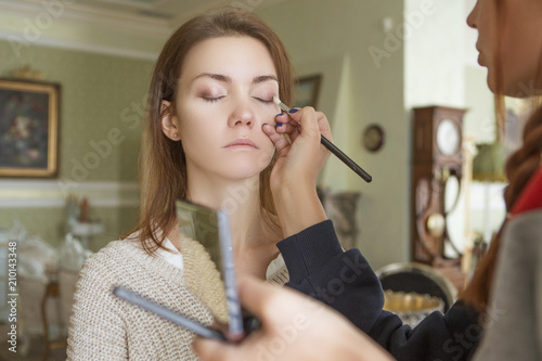 Brunette make up artist woman applying make up for a caucasian brunette bride, preparing her for a wedding photosession or a date