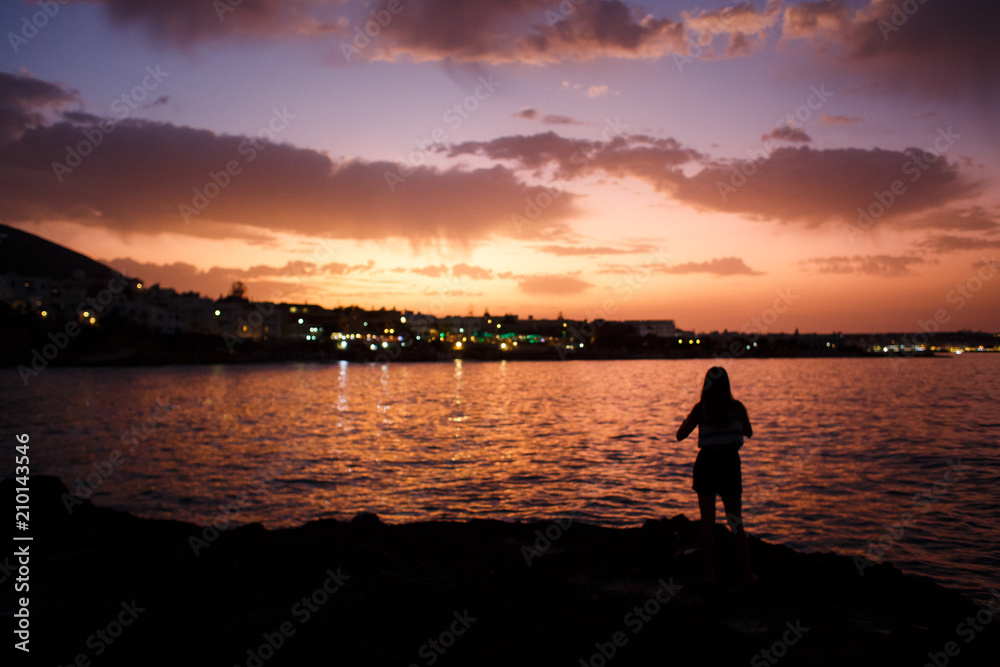 Silhouette of a girl who admires the beautiful sunset by the sea
