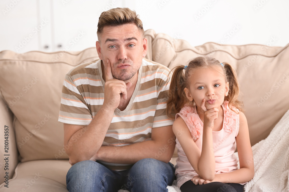Funny father and daughter sitting on sofa at home