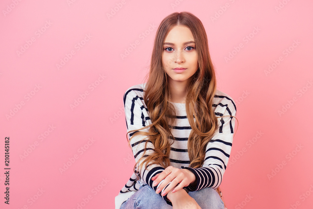 portrait of a young and attractive teenager long-haired woman stylish model posing in a striped sweater in studio on a pink background portrait of a young and attractive teenager long-haired woman stylish model posing in a striped sweater in studio on a pink background