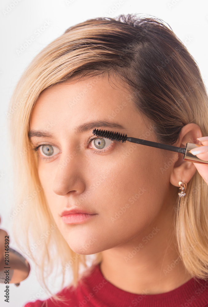 Young beautiful woman applying mascara makeup on eyes by brush