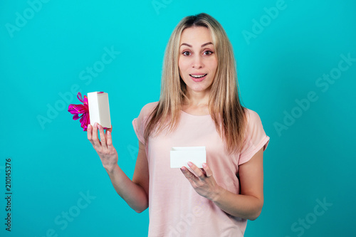 cheerful attractive surprised and shocked woman smiling and holding a box with a gift on a blue background in the studio.