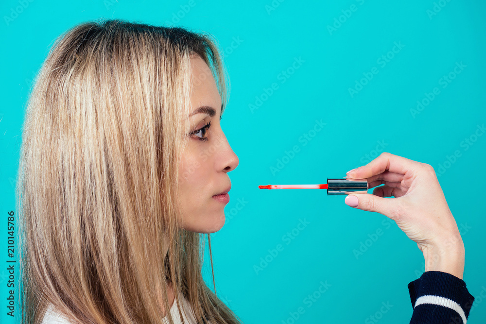 young and attractive blonde woman visagiste (make-up artist ) beauty blogger is applying makeup lipstick on lips on blue background in a studio. concept of skin care and beauty cosmetics for face
