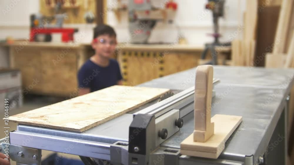Carpenter makes wood processing in the workshop and little boy watching and learning at background Carpenter makes wood processing in the workshop and little boy watching and learning at background