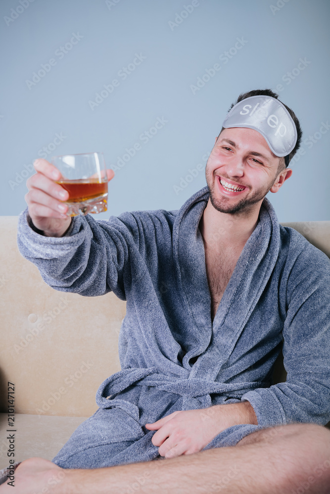 Happy young man in dressing gown drinking whiskey.Drunk man drink alcohol lying in sofa.the guy after the stag party