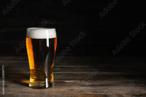 Glasses with cold beer on wooden table against dark background